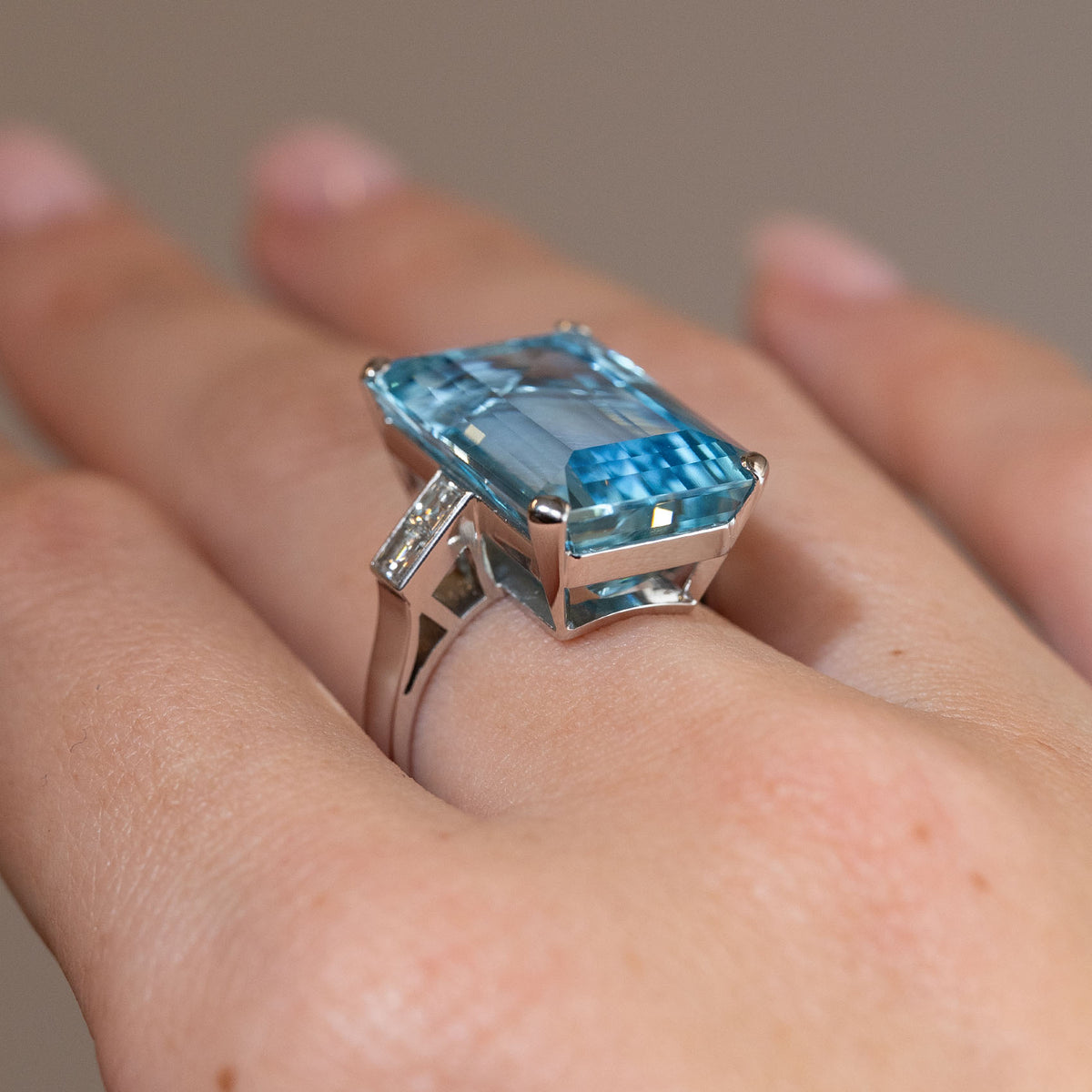 Side profile of a vintage 1970s aquamarine cocktail ring worn on a finger, revealing its raised open setting, diamond-set shoulders and white gold band.
