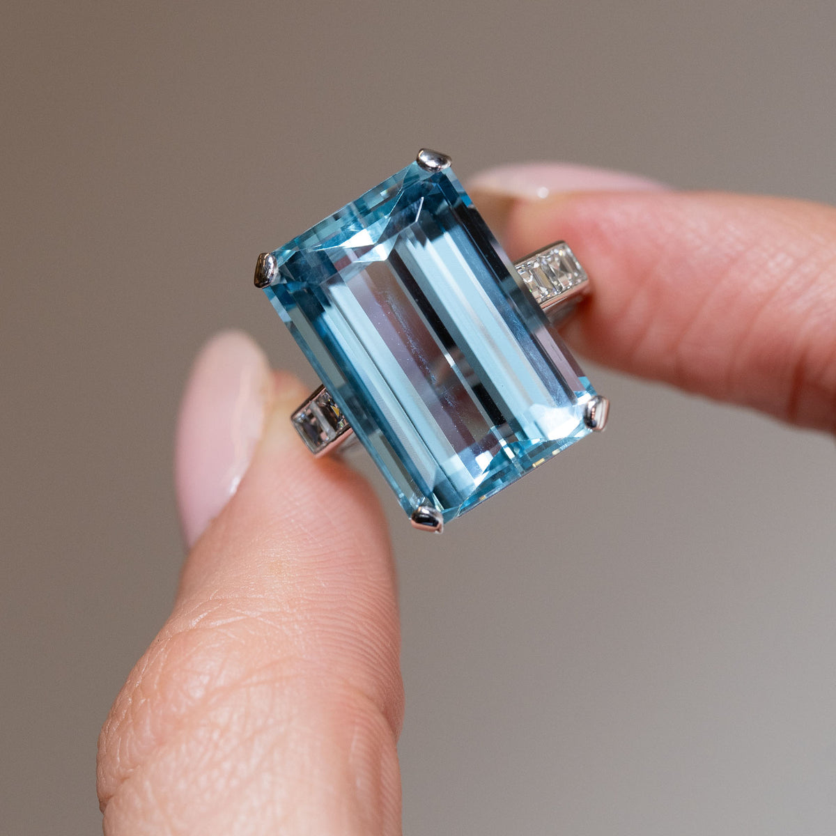 Detailed close-up of a vintage 1970s aquamarine and diamond cocktail ring held between fingers, highlighting the aquamarine's crisp step-cut facets and four-claw setting.