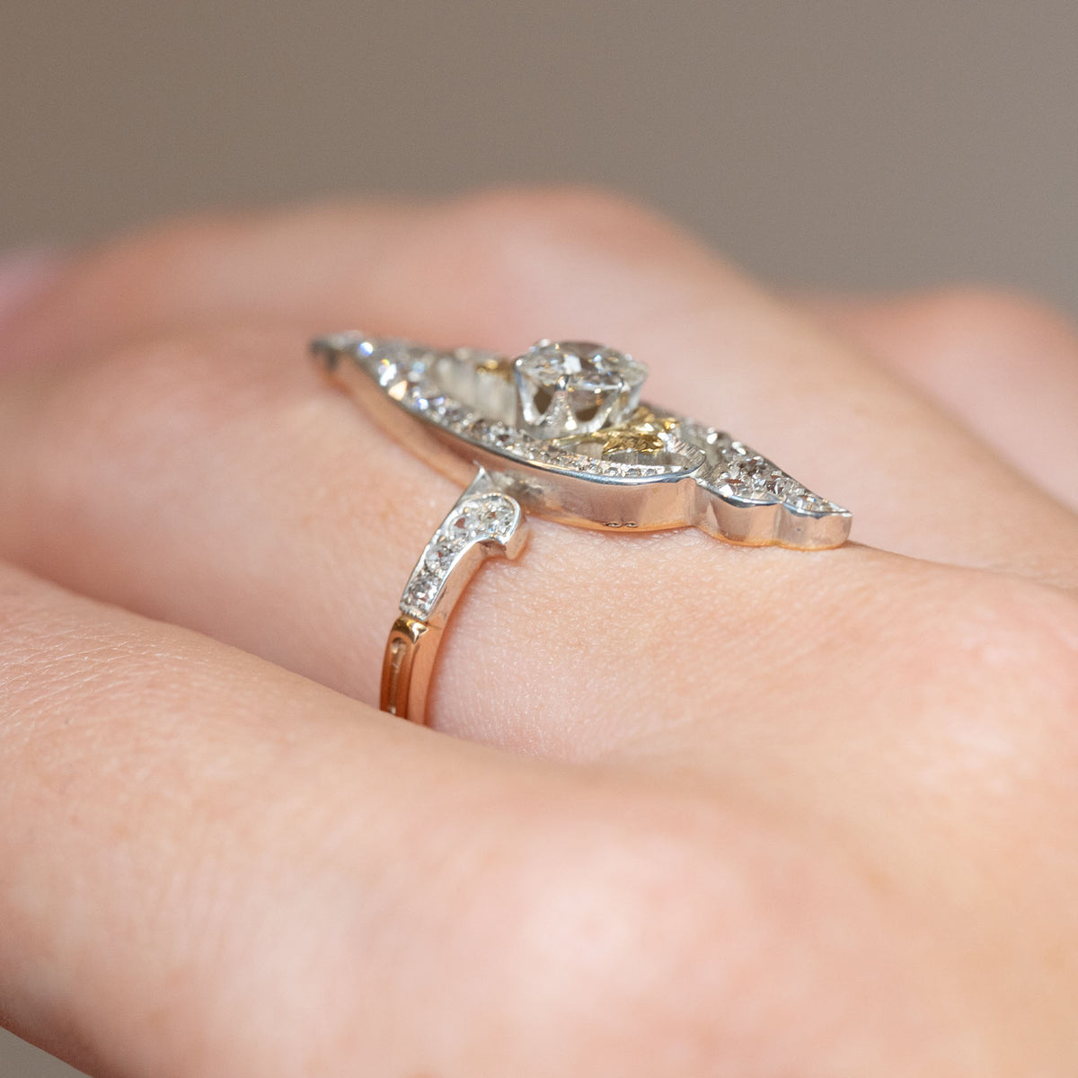 Side profile of an antique Art Nouveau diamond cross-over ring worn on the finger, displaying its raised setting and sculptural design.