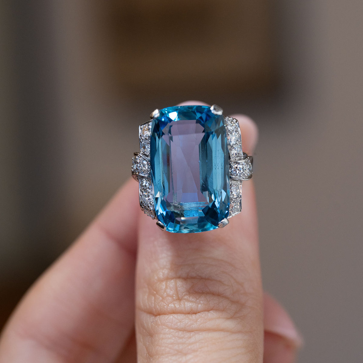 Hand-held close-up of the vibrant blue aquamarine, framed by sparkling diamonds in an elegant Art Deco platinum setting.