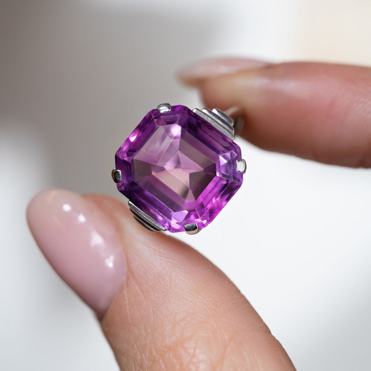Hand-held close-up of the large purple amethyst, showcasing its octagonal emerald cut and intricate white gold setting.