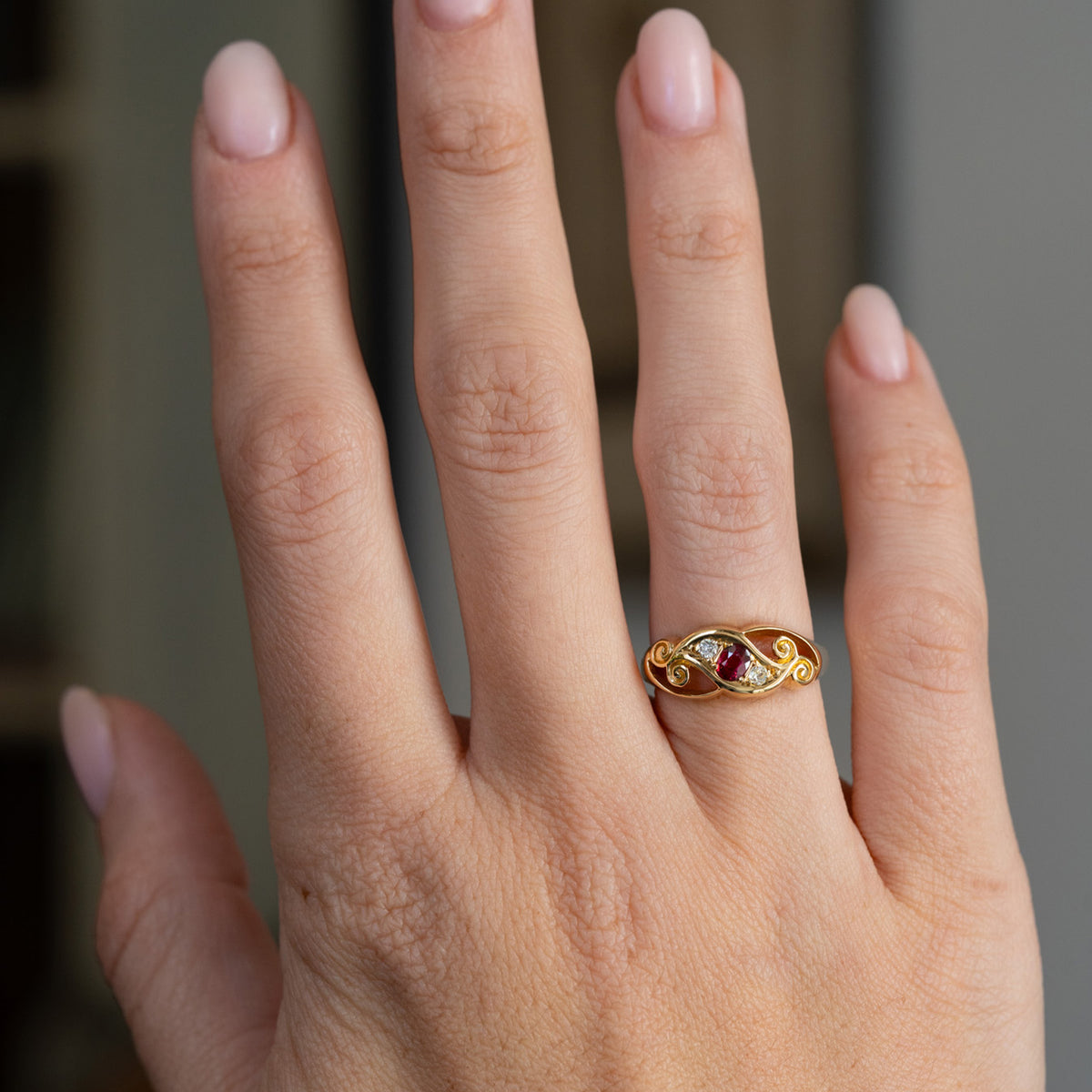 Edwardian ruby three-stone ring worn on the hand, showing the distinctive width and sculptural shape of its yellow gold setting.