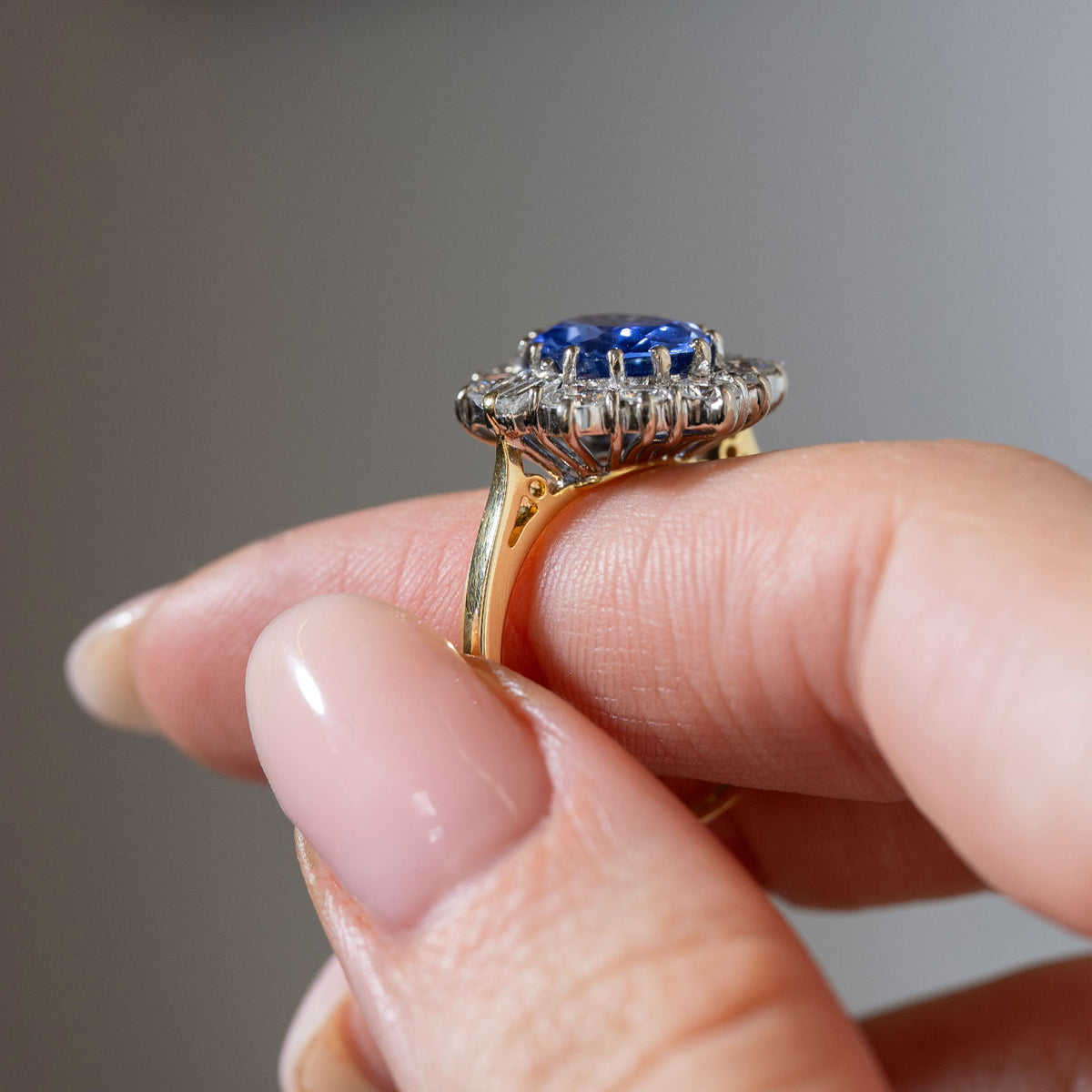 Side profile of a vintage 1980s blue sapphire and diamond cluster ring held between fingers, showing the elevated platinum cluster setting, diamond gallery and yellow gold band.