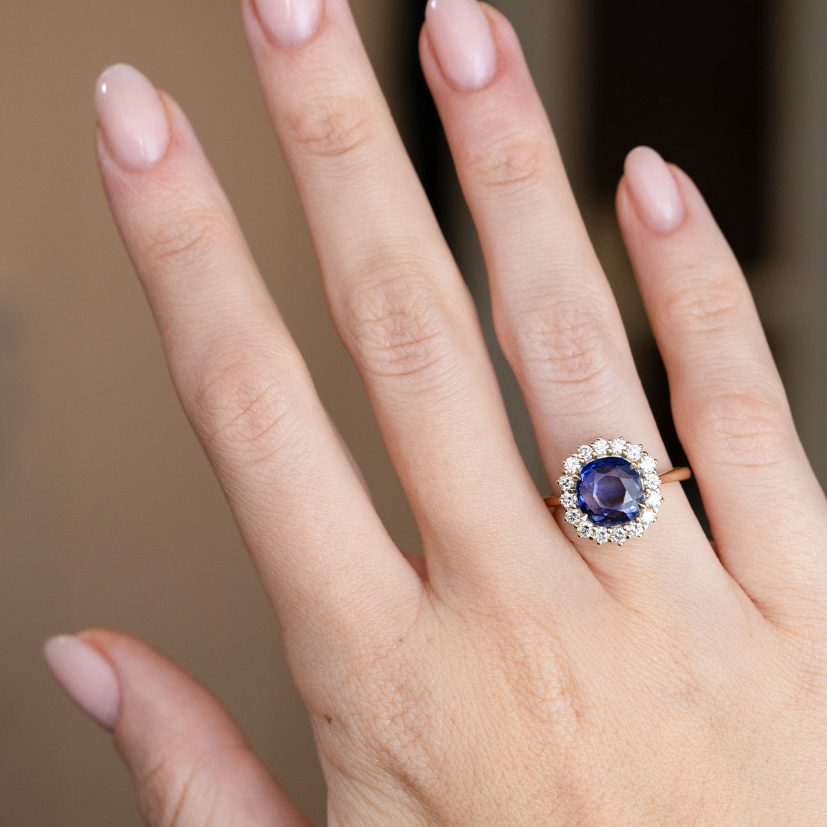 An elegant sapphire and diamond halo ring shown on a hand, demonstrating its proportions and striking oval centre stone.