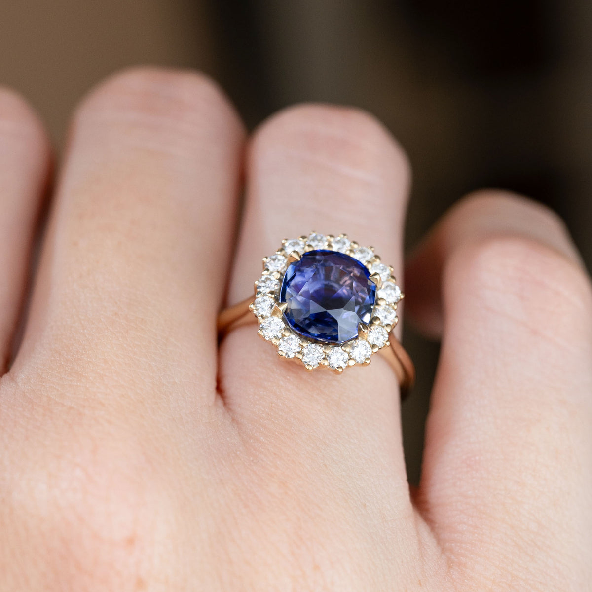 The vintage-style blue sapphire ring worn on a finger, with a dazzling diamond halo creating a classic floral-inspired design.