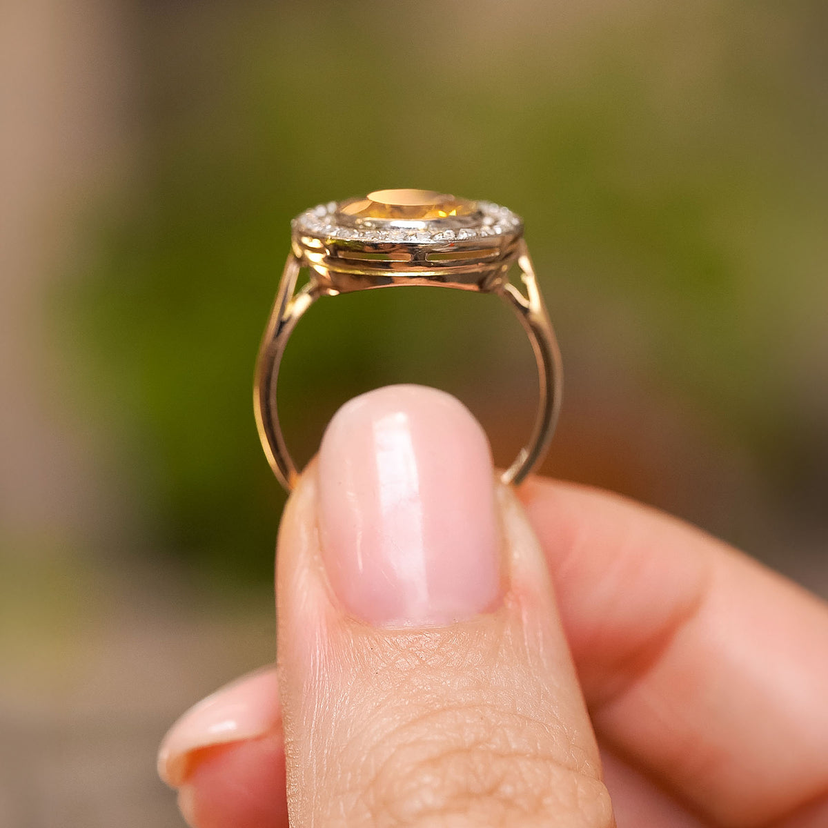 Profile view of a Belle Époque citrine ring held between the fingers, revealing its elevated platinum setting and yellow gold shank.