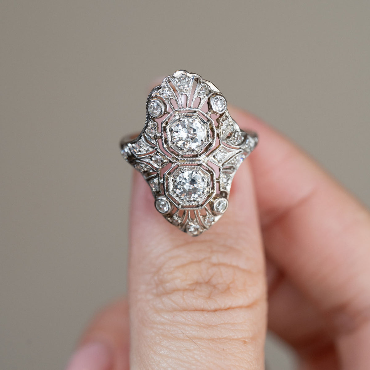 Detailed front view of the Art Deco cocktail ring held between fingers, highlighting the two central diamonds and beautifully symmetrical openwork.