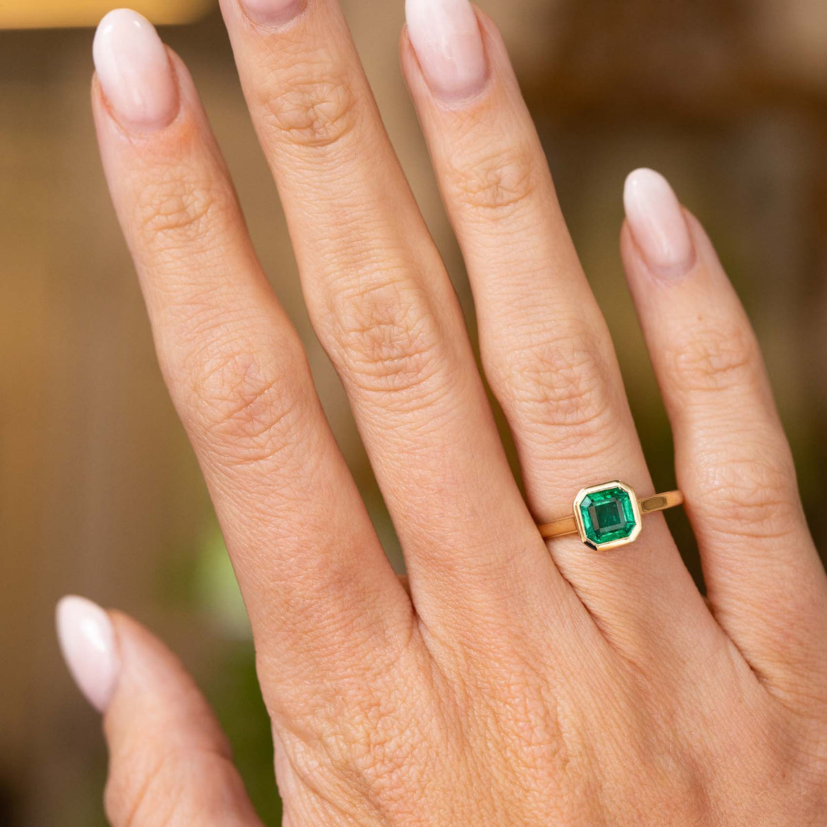 A close-up of a hand wearing an Antique-inspired, Emerald solitaire engagement ring in yellow gold.