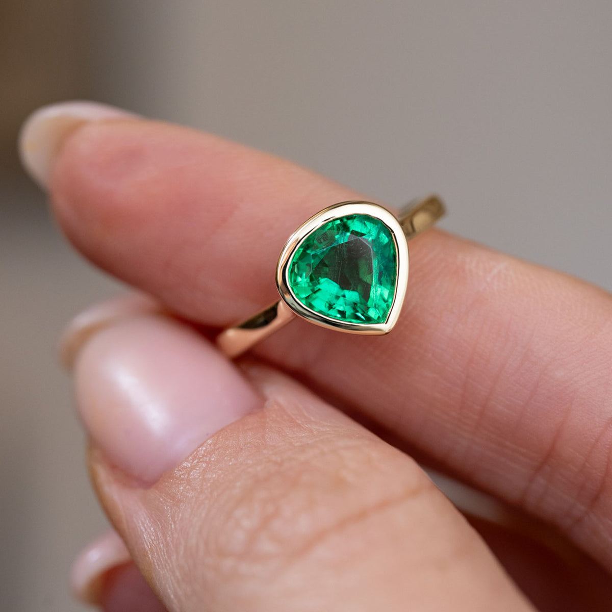 Handheld close-up of the pear-cut emerald solitaire, capturing its rich green colour and sleek yellow gold surround.