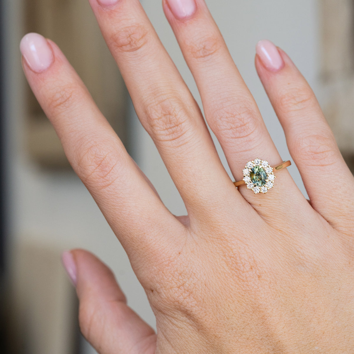Worn on the hand, this yellow gold engagement ring displays the rich pine green sapphire and its classic oval diamond surround.