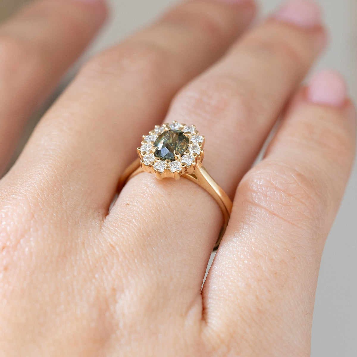 Oblique hand detail revealing the raised yellow gold setting, oval sapphire centre and sculptural round diamond cluster.