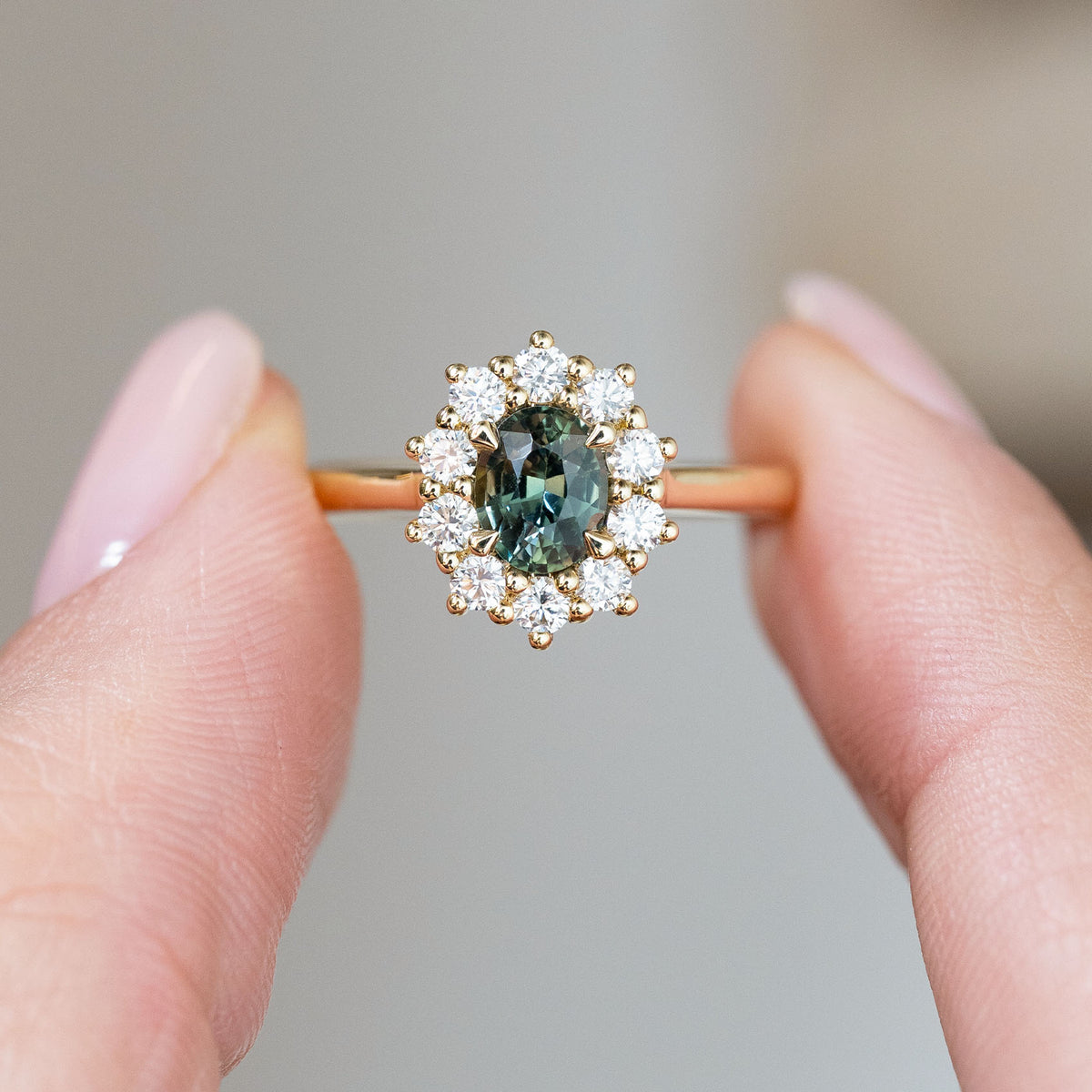 Held between the fingers, the engagement ring’s green sapphire centre and symmetrical round diamond cluster come into sharp focus.