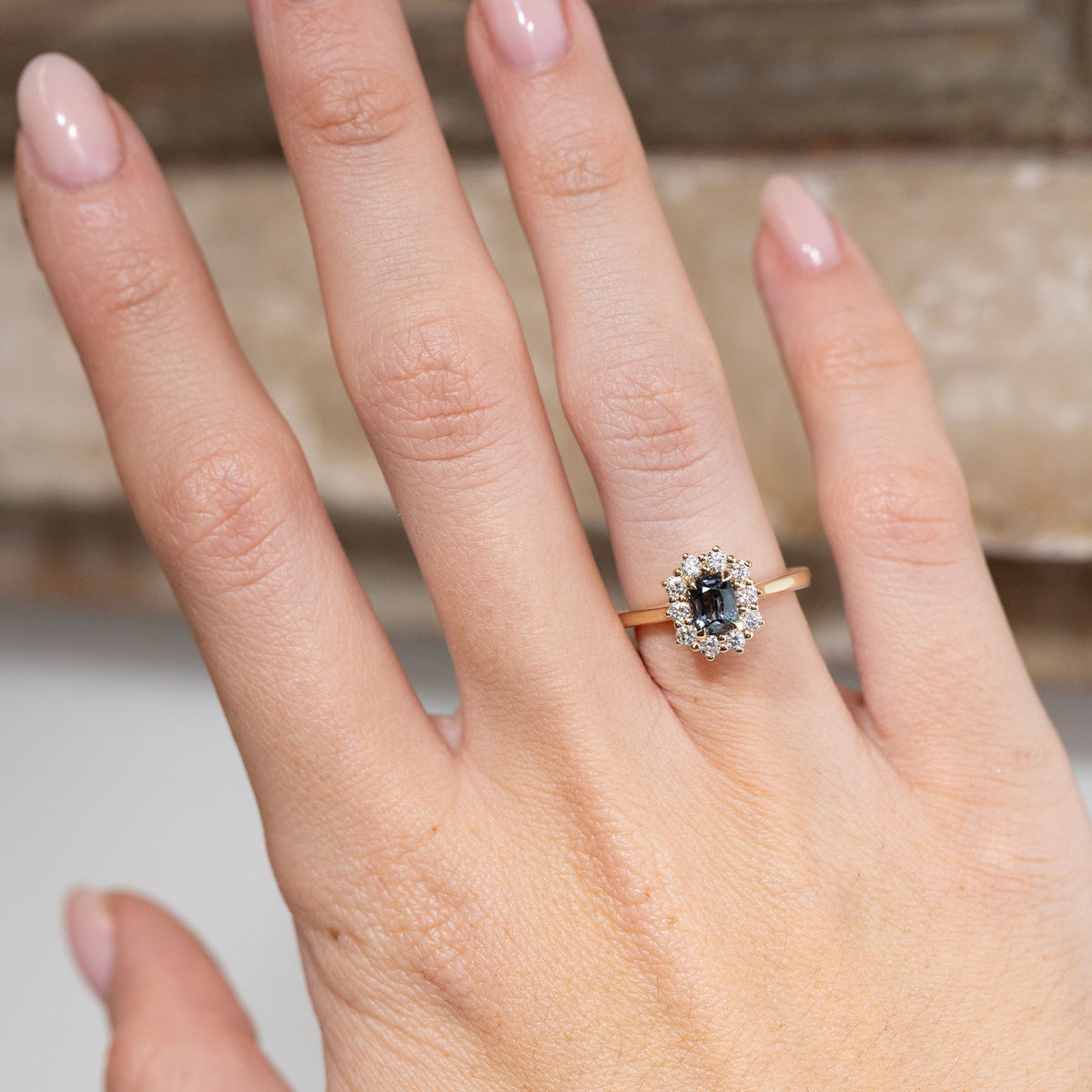 Blue sapphire and diamond engagement ring worn on a hand, showcasing its deep blue-green gemstone and elegant cluster design.
