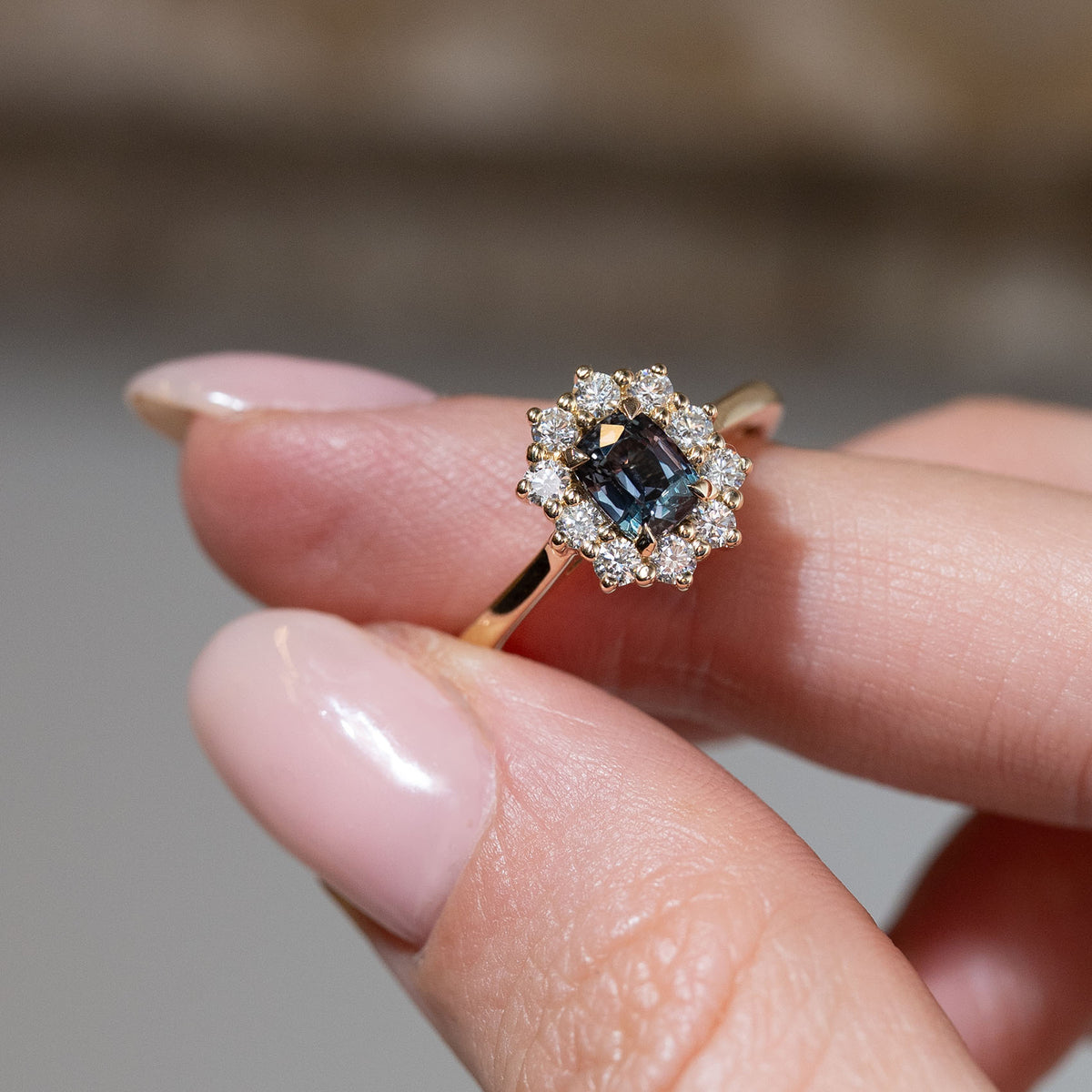 Hand-held close-up of the dark blue sapphire surrounded by sparkling white diamonds in an antique-inspired yellow gold setting.