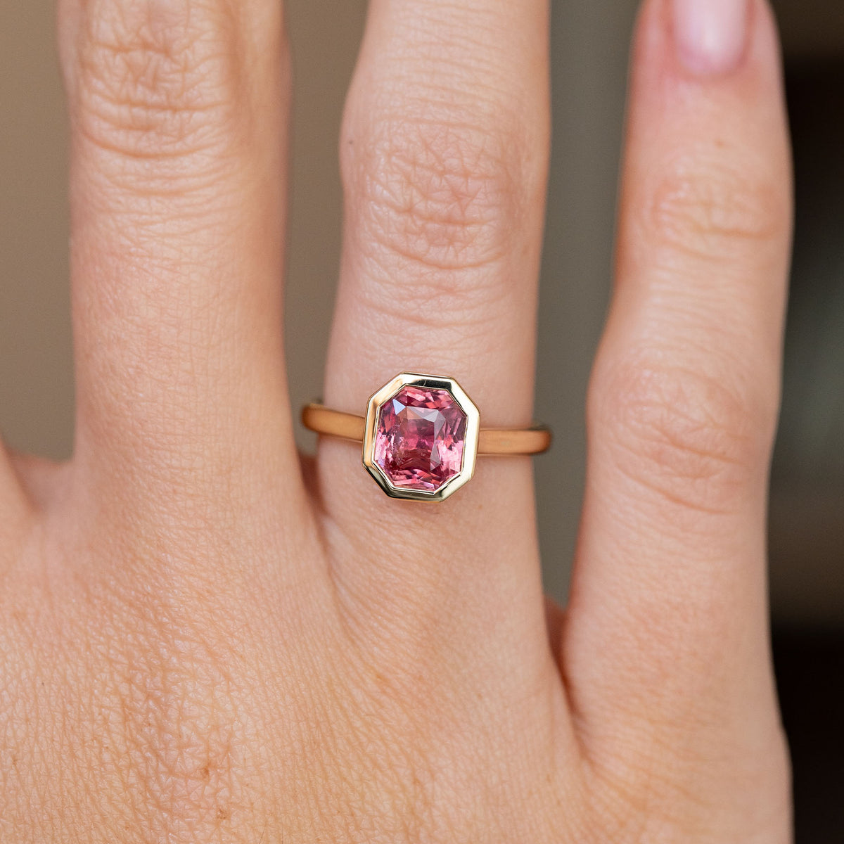Close-up on-hand view of the faceted pink sapphire framed by a sleek geometric yellow gold surround.