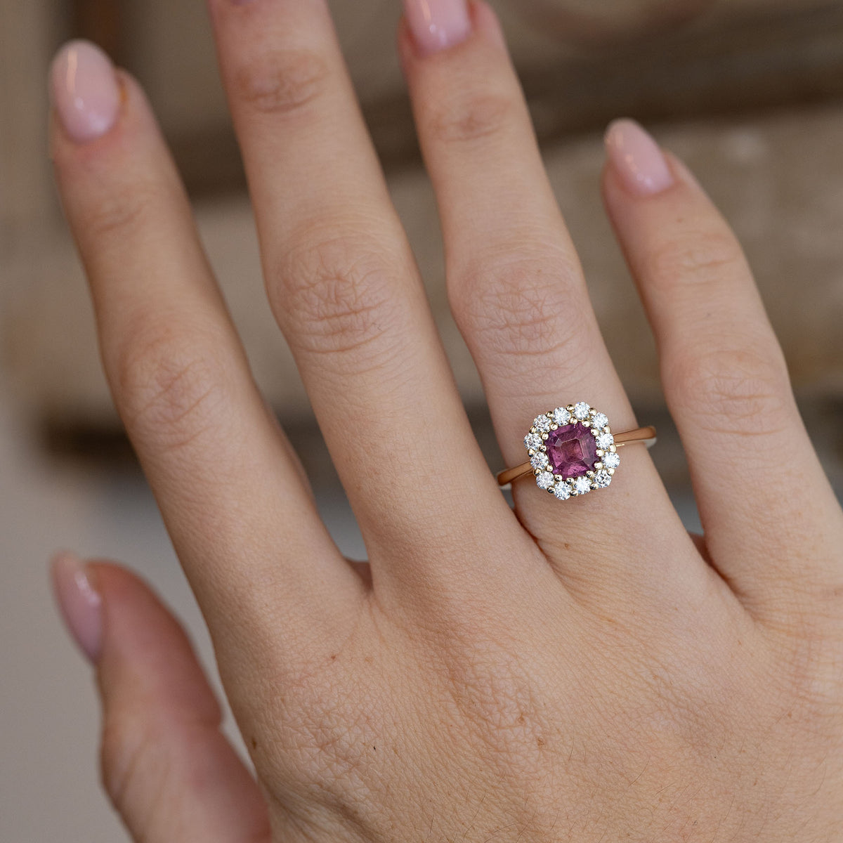 Pink sapphire and diamond engagement ring worn on a hand, showcasing its rich pink gemstone and elegant cluster design.