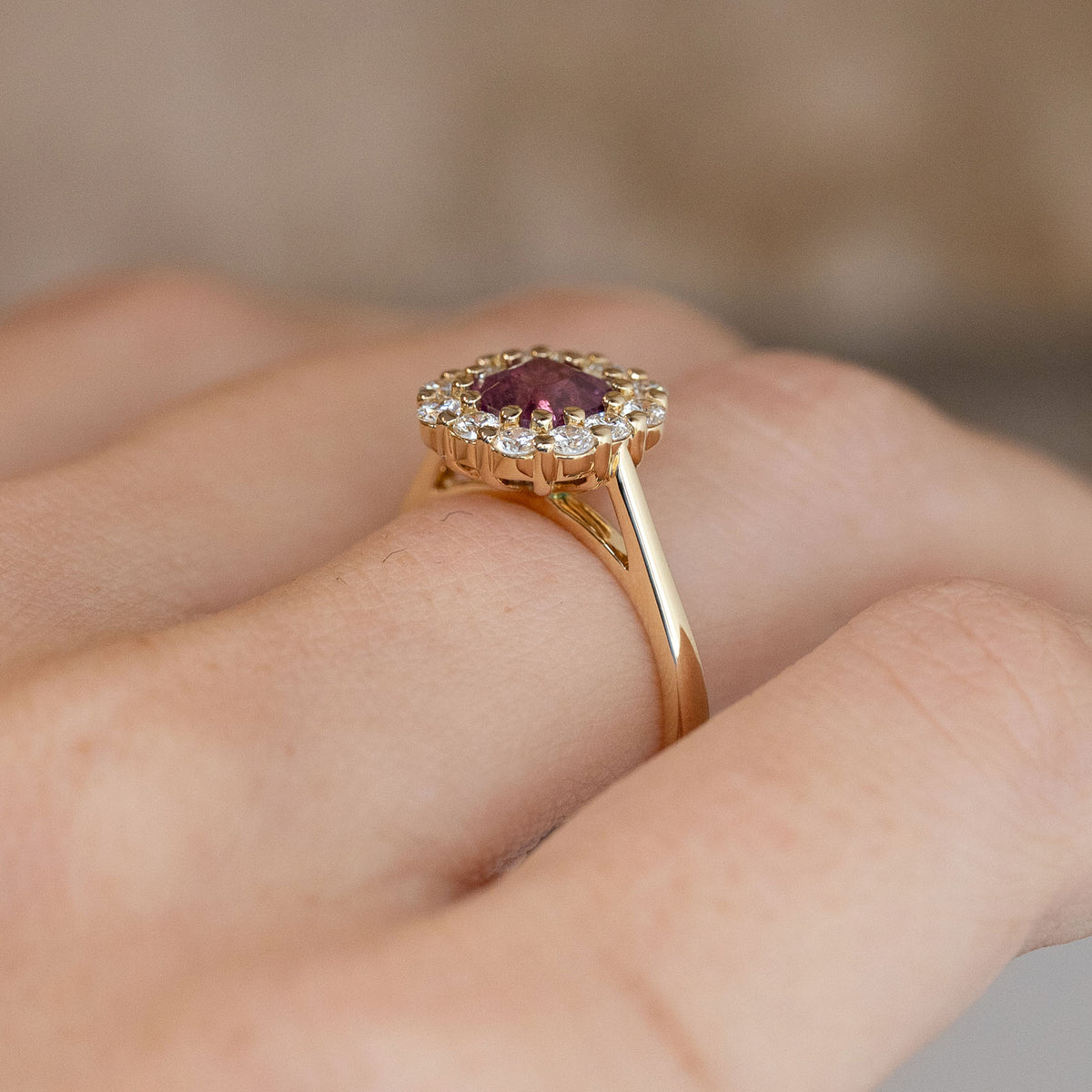 Side-angle view of the pink sapphire ring worn on a hand, highlighting the elevated cluster setting and delicate yellow gold band.