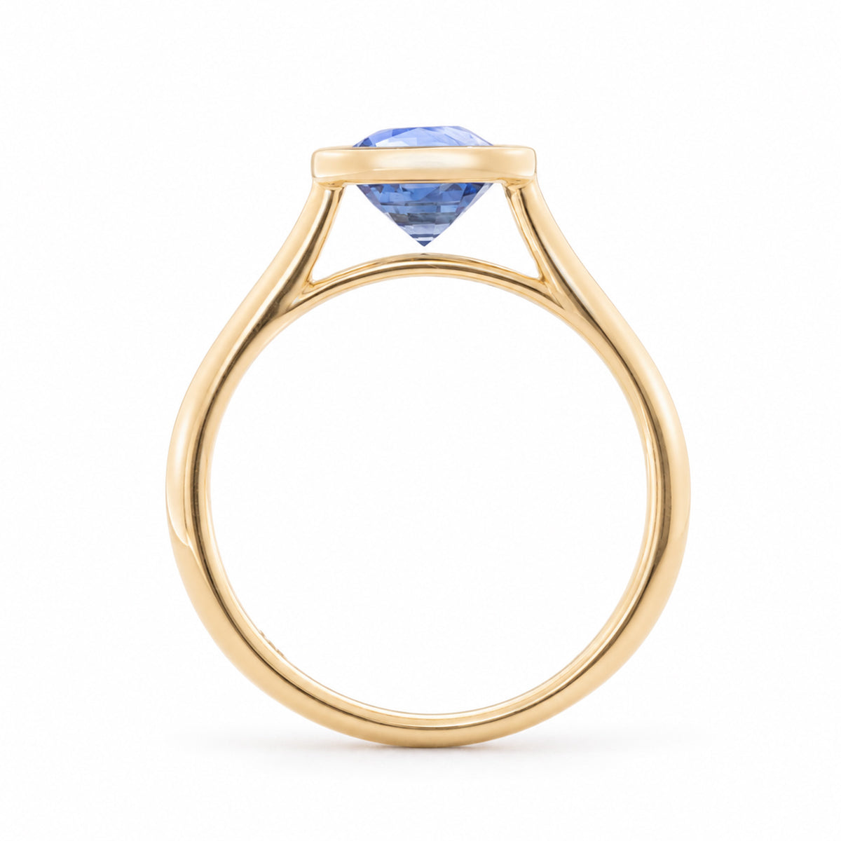 Side profile of the blue sapphire solitaire ring, highlighting the raised bezel setting and open gallery in yellow gold.