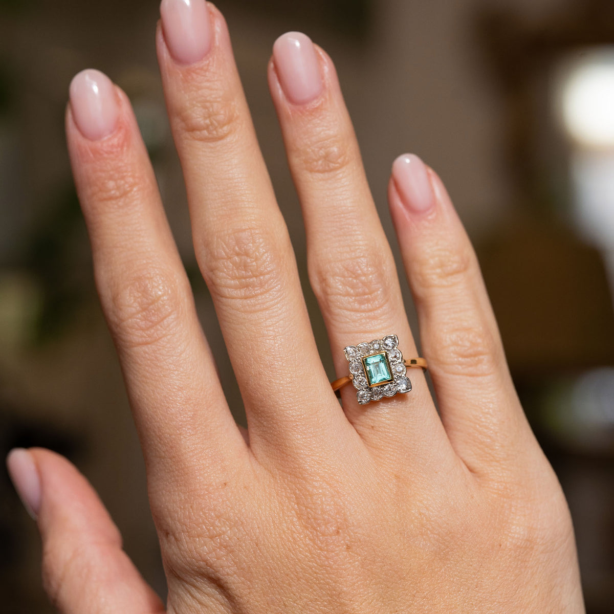 Full-hand view of an Edwardian emerald cluster ring, featuring a step-cut mint green centre stone framed by antique diamonds.