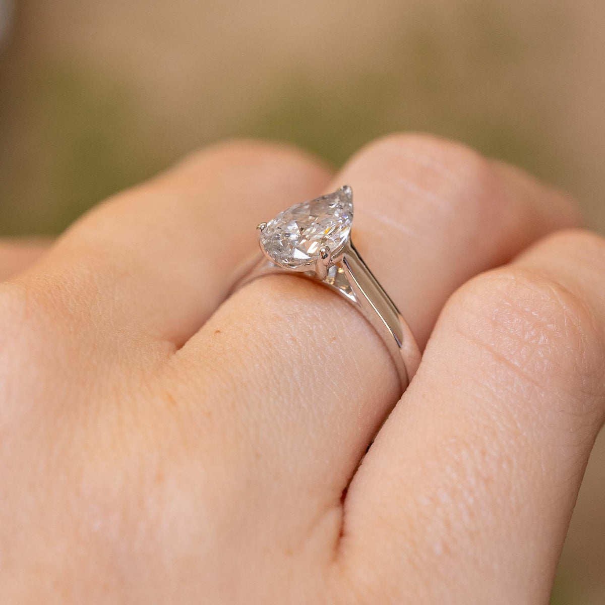 Side view of a vintage pear-cut diamond solitaire worn on the hand, revealing its raised claw setting and tapered shoulders.