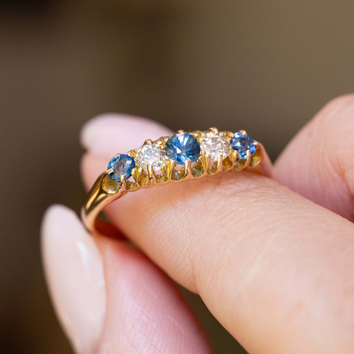 Side detail of an antique Edwardian sapphire and diamond five-stone ring held between the fingers.