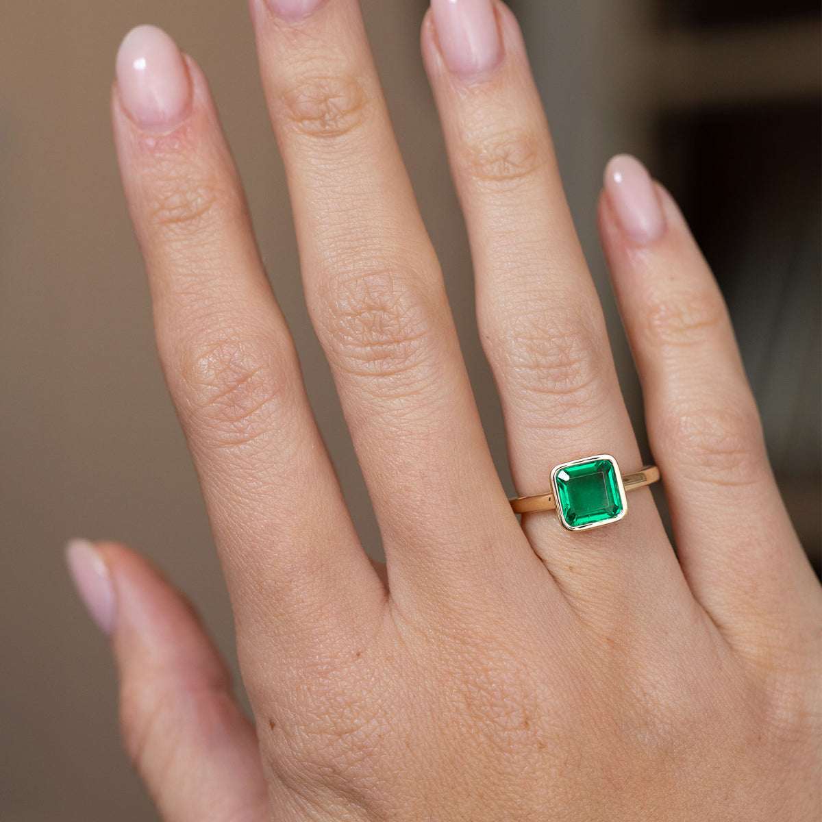 Antique-inspired emerald engagement ring worn on the hand, showing the elegant proportions of its square solitaire design.