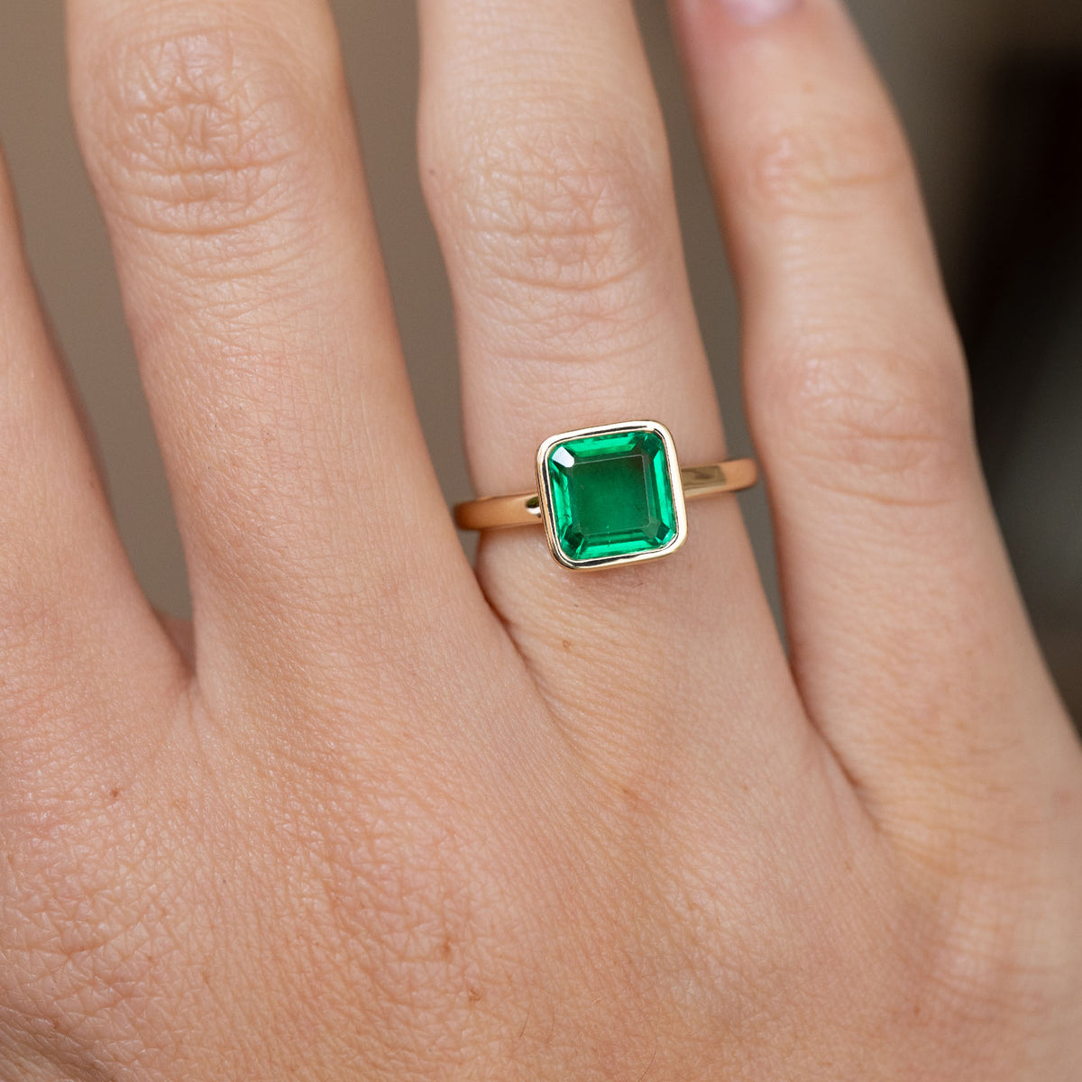 Close-up of the square emerald-cut Colombian emerald and sleek yellow gold setting on the finger.