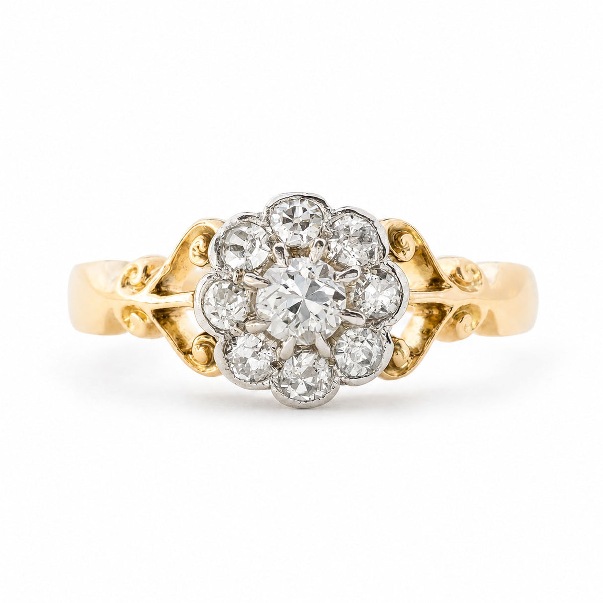 An Antique Edwardian era diamond daisy cluster engagement ring set in yellow gold with ornate scrollwork photographed on a clean white background.