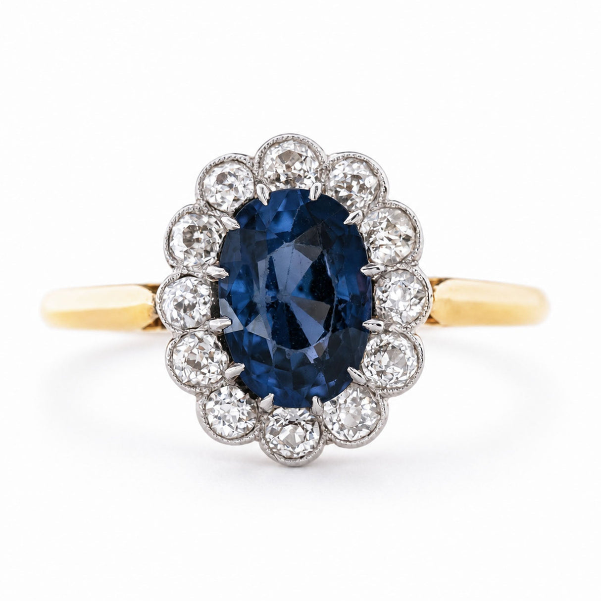 an Antique, Edwardian blue spinel oval-cut and diamond cluster engagement ring mounted on a yellow gold band and shown against a white background.