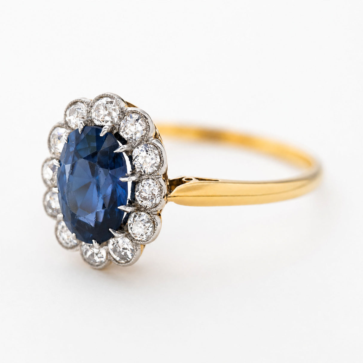 An image of an Antique, Edwardian deep blue spinel and diamond cluster engagement ring on a yellow gold band turned to the side and shown against a white background.