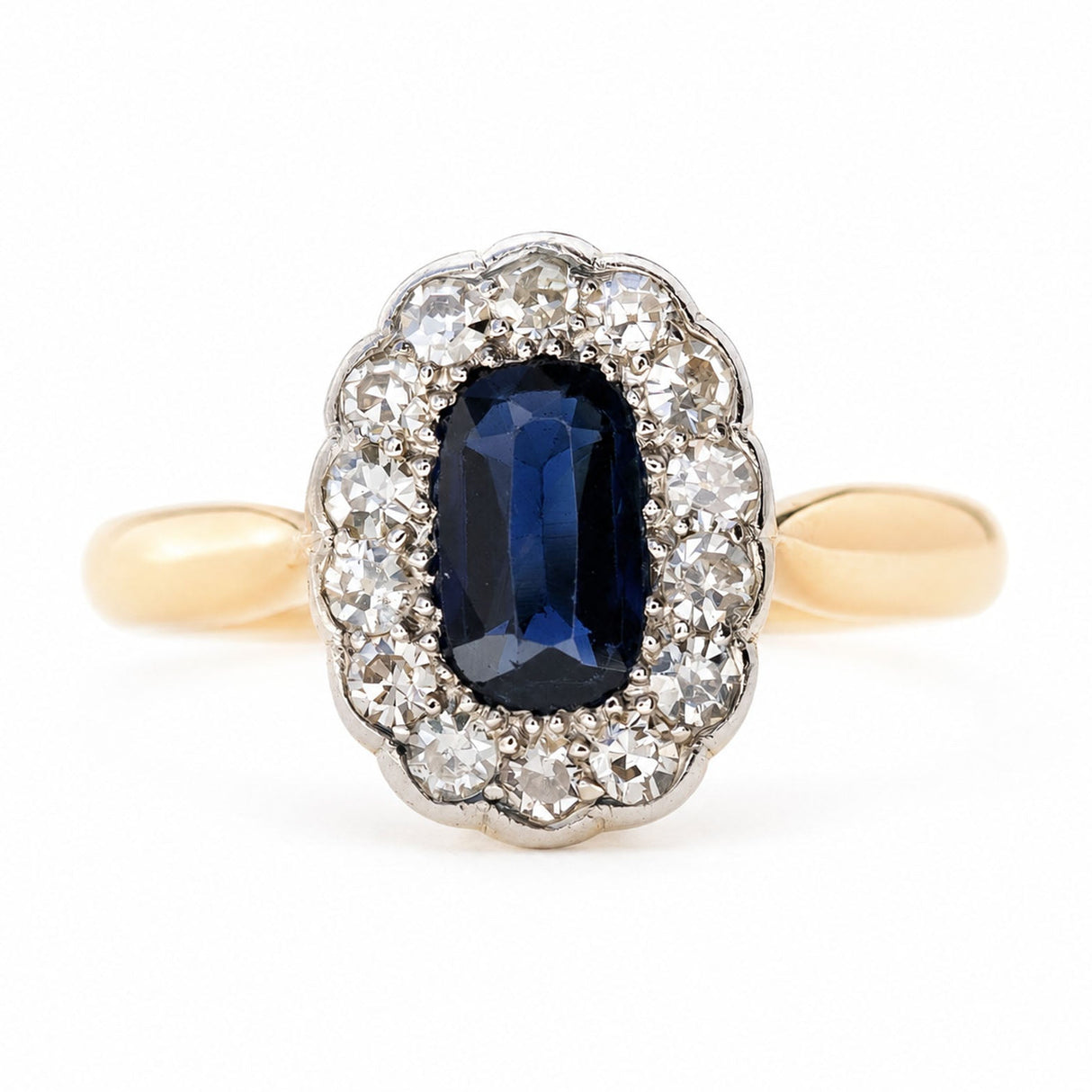 An Antique Edwardian Sapphire and Diamond Cluster engagement Ring set on a yellow gold band, photographed on a white background.
