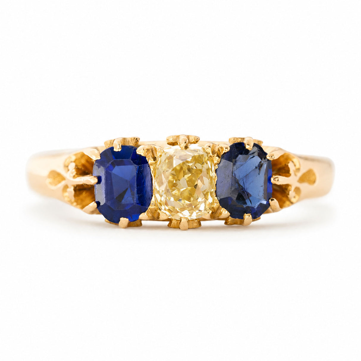 A yellow gold Antique, Victorian blue sapphire and yellow diamond three-stone engagement ring seen against a white background.