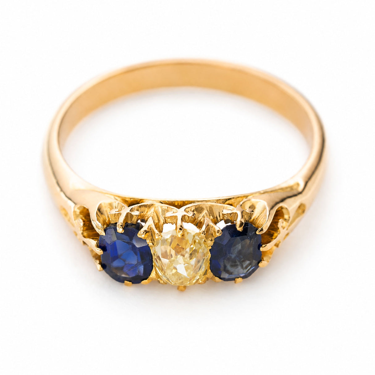 An Antique yellow gold Victorian blue sapphire and yellow diamond trilogy engagement ring shown against a white background from above to show off the claw settings.