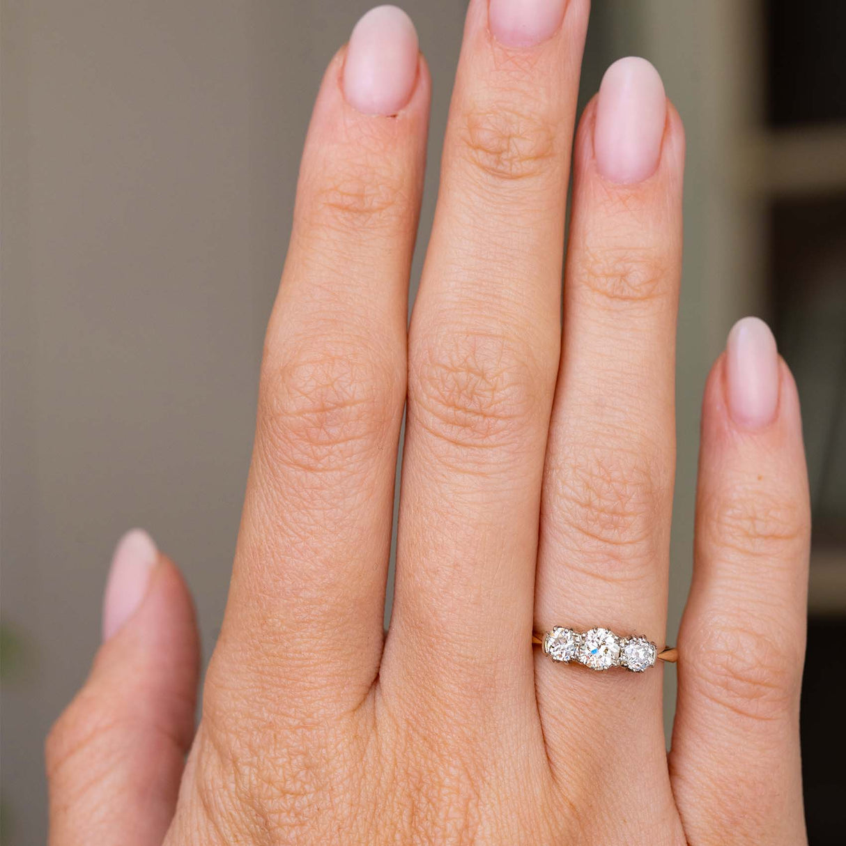 A hand wearing an Antique, Edwardian diamond three-stone engagement ring in yellow gold.