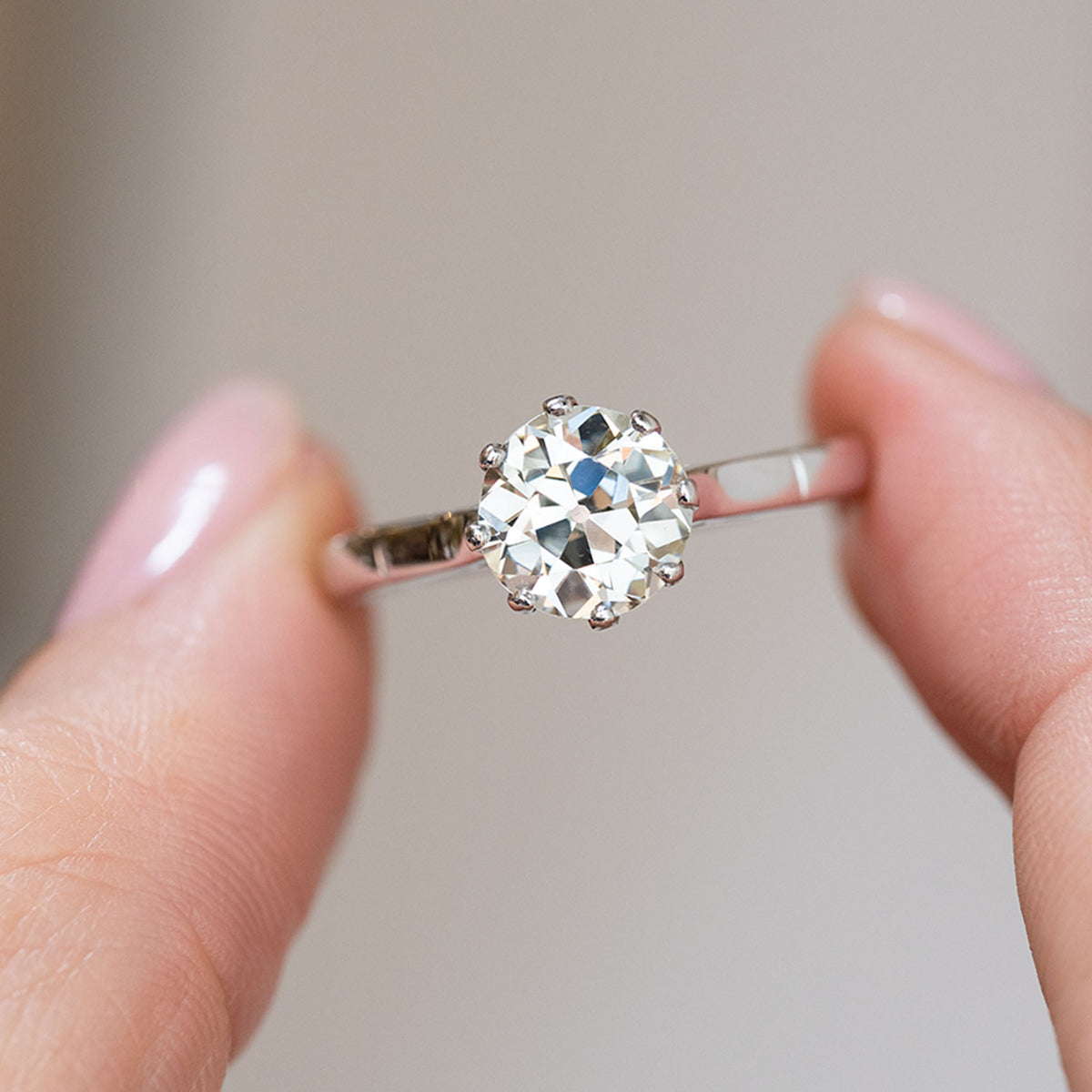 Warm old-cut diamond ring held between the fingers, offering a detailed look at its broad facets and antique charm.
