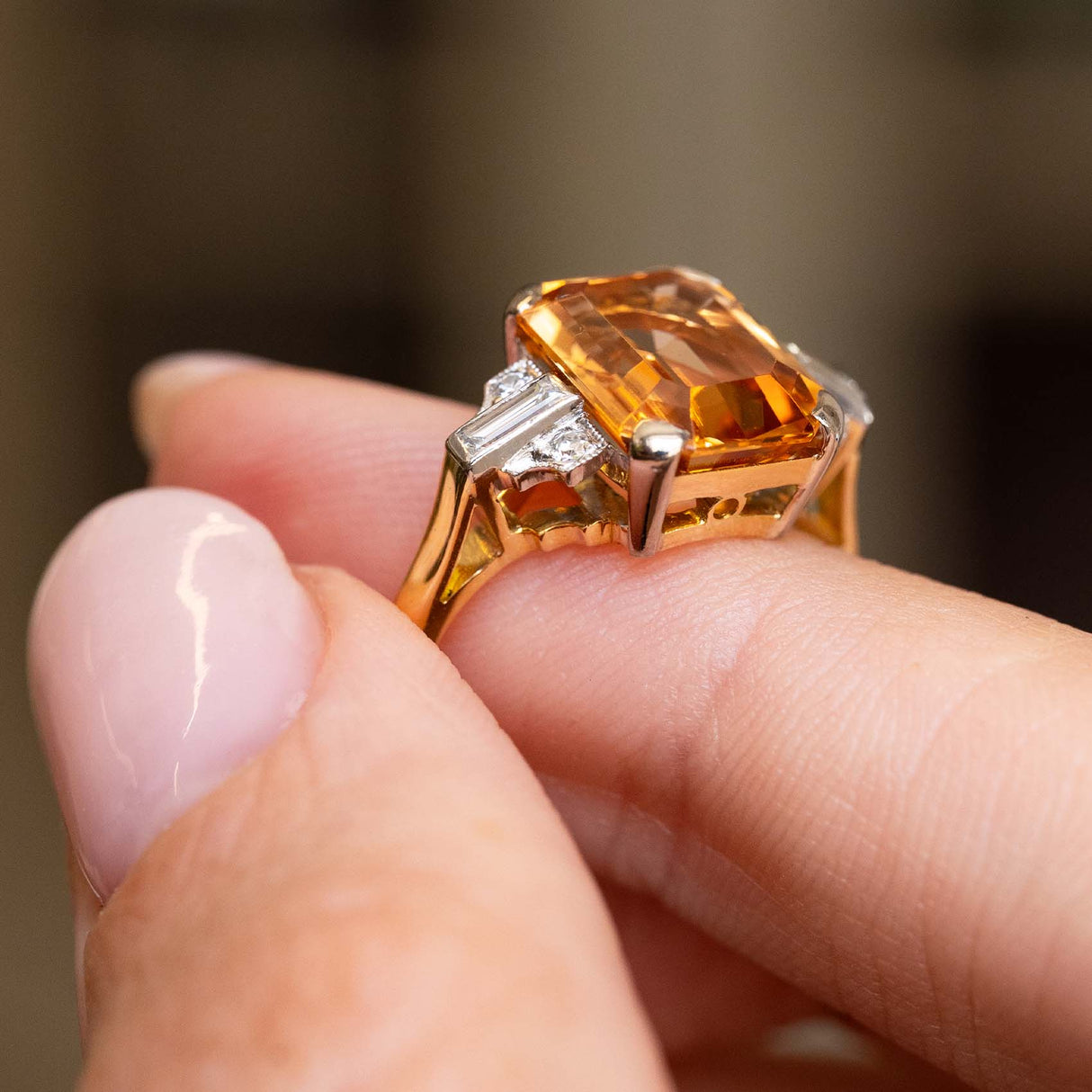 A close-up of a hand wearing a gold Vintage, 1950s Sherry topaz and diamond cocktail ring shown against a blurred background.
