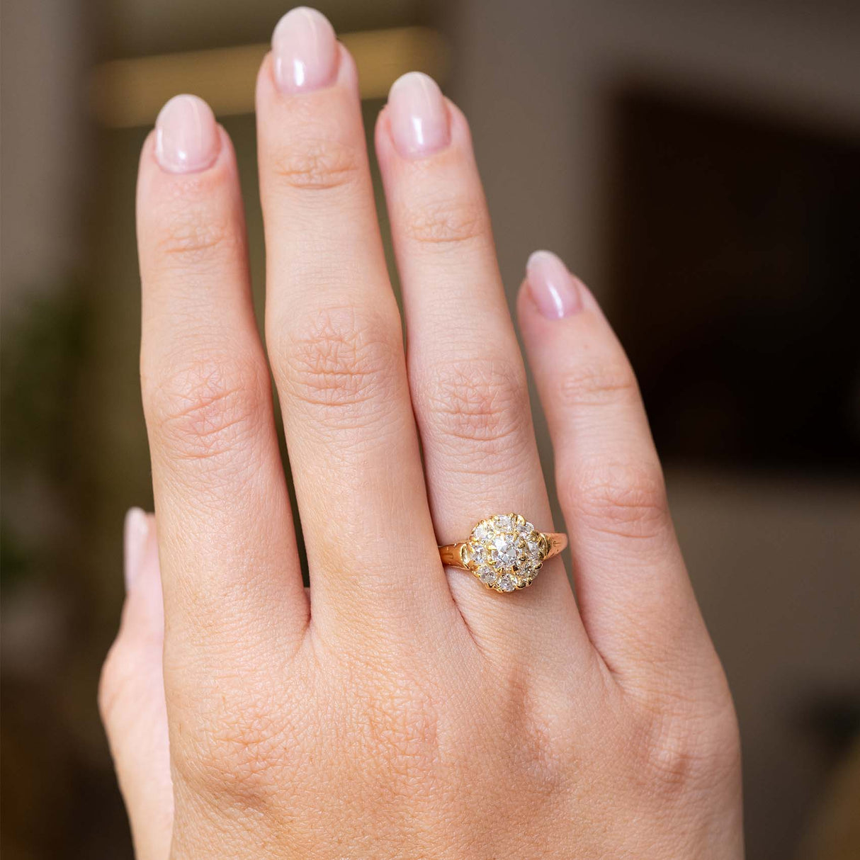 An outstretched hand wearing an antique Victorian era yellow gold old-cut diamond coronet cluster engagement ring, seen from a distance to show its proportions and scale.