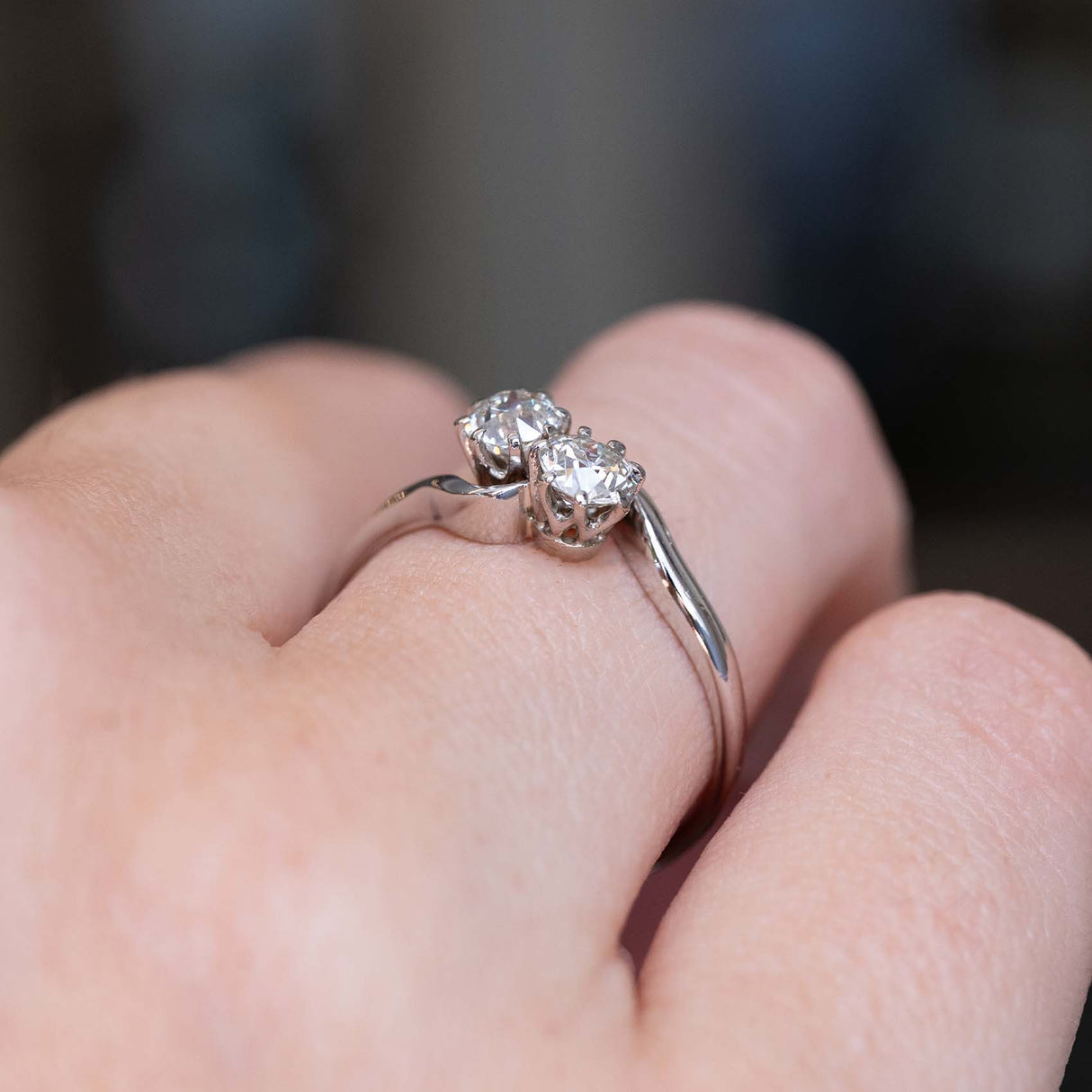 A close-up image of an Antique, Edwardian toi et moi diamond engagement ring in platinum worn on a person's finger seen from a low angle to show the setting style of the diamonds.