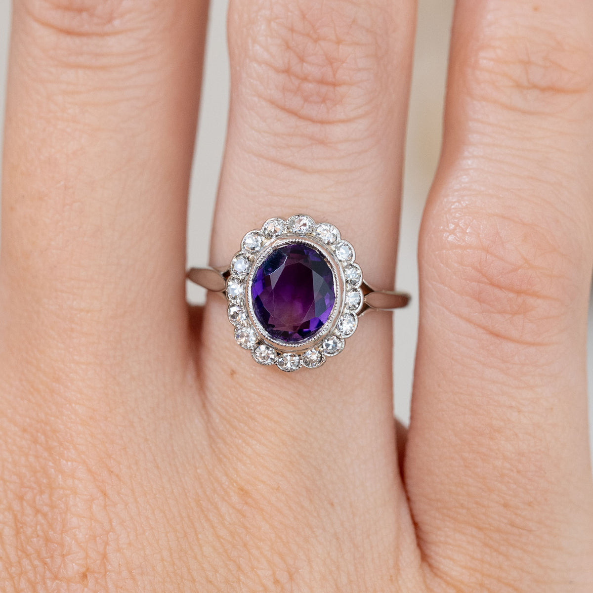 An intimate hand close-up captures the purple amethyst’s faceting and the delicate platinum-set diamond surround.