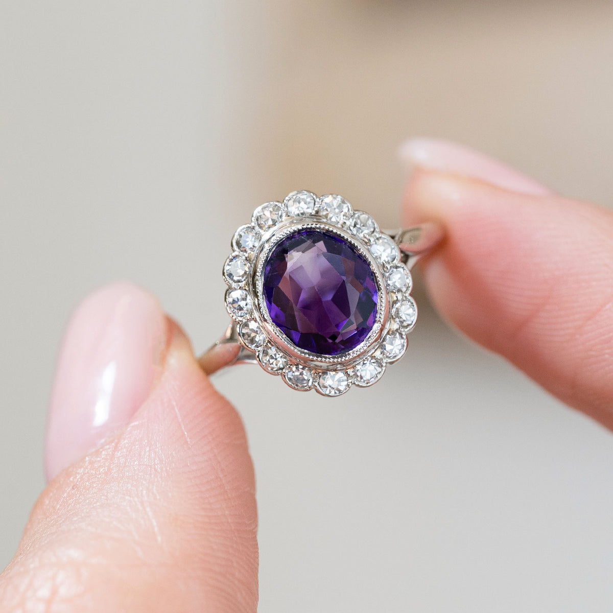 Held between the fingers, the amethyst’s deep violet tones sit prominently within a luminous halo of old-cut diamonds.