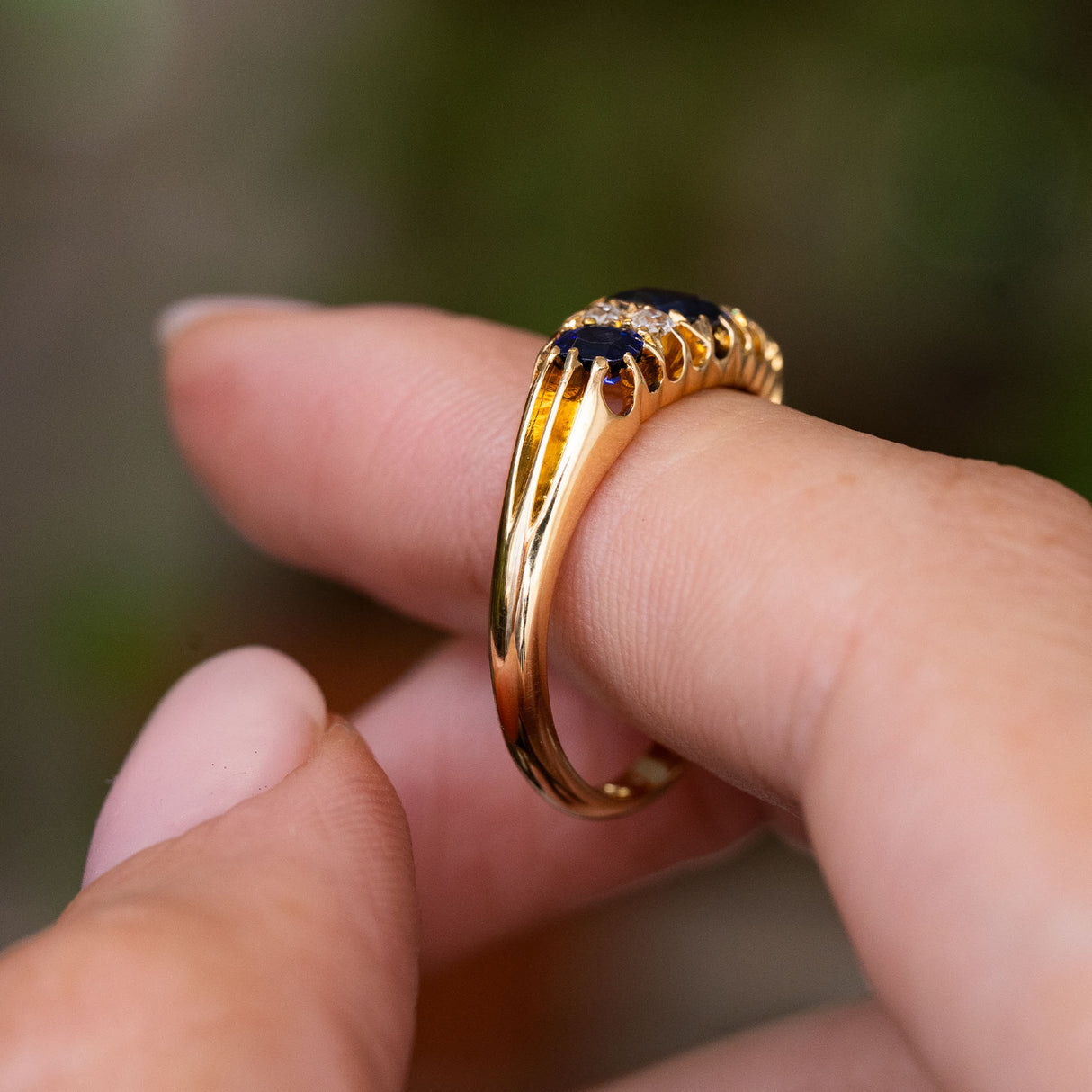 Side profile of an Antique, Edwardian blue sapphire and diamond five-stone engagement ring displaying the detailing on the shoulders and the low profile of the ring and yellow gold band.