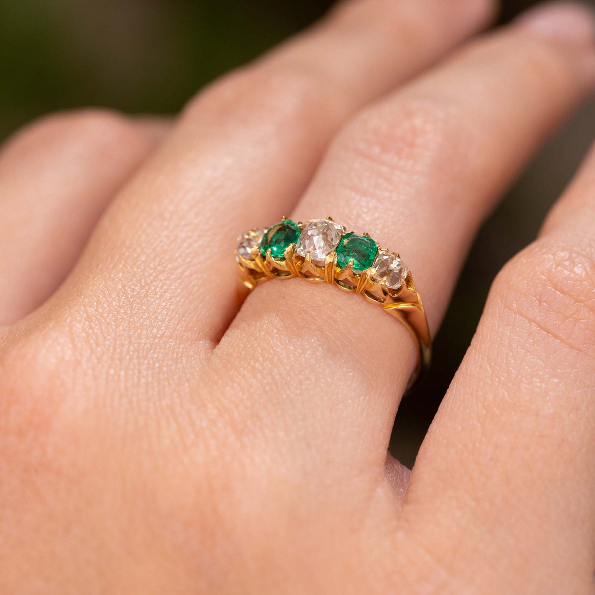 A close-up of a hand wearing an Antique, Victorian emerald and diamond five-stone engagement ring in yellow gold.