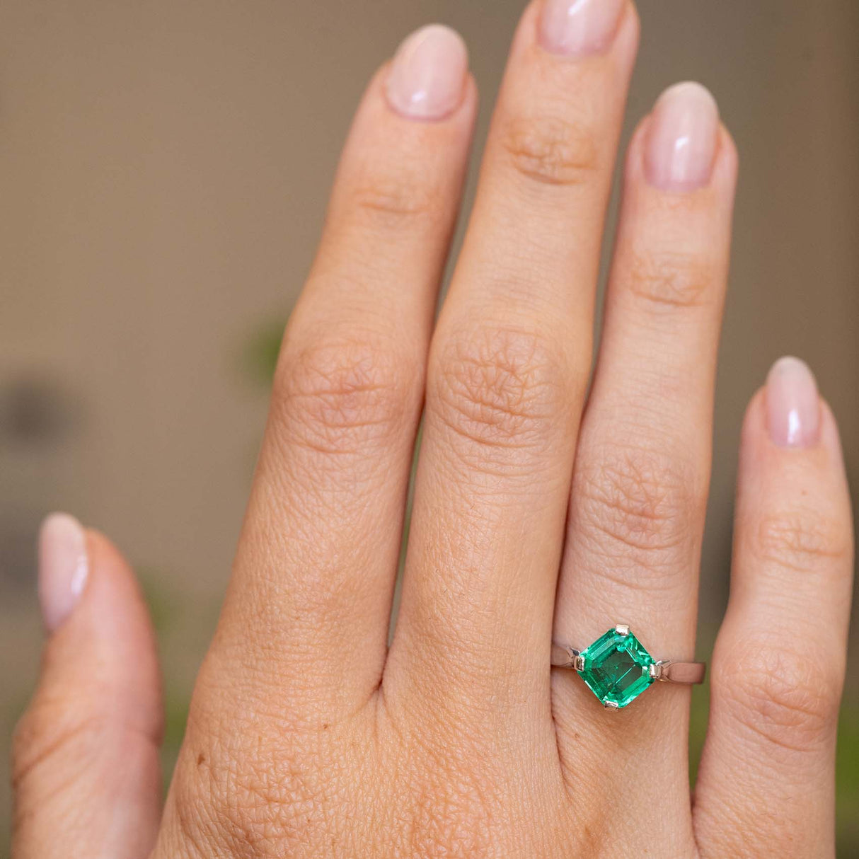 A close-up of a hand wearing a Vintage, 1990s square-cut emerald solitaire unique engagement ring in white gold.