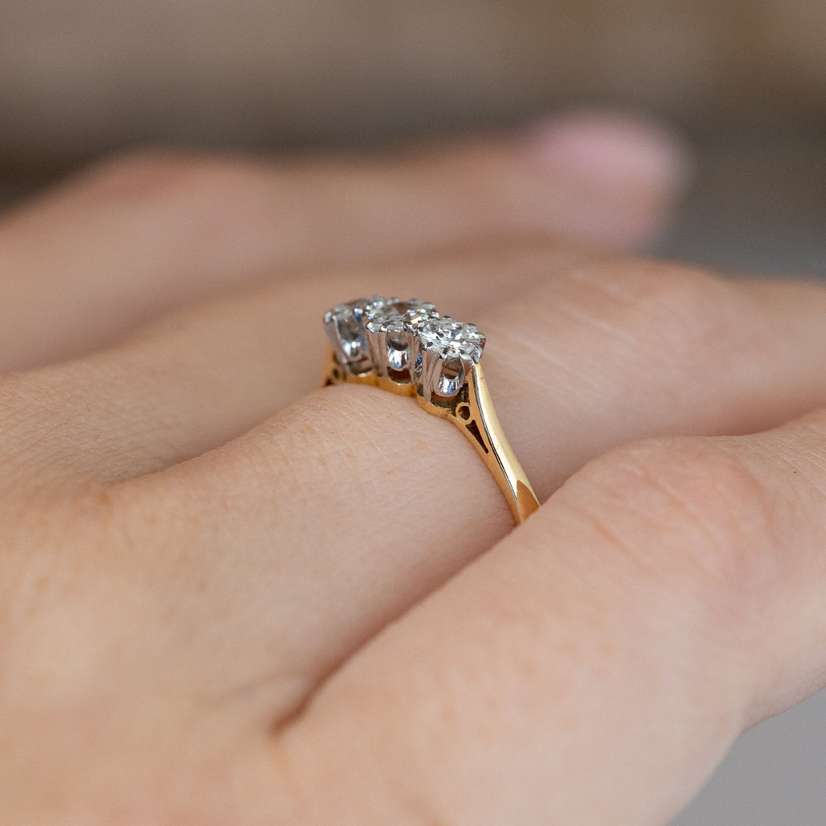 Side-angle view of the Edwardian three-stone ring worn on a hand, highlighting the elevated platinum settings and yellow gold band.