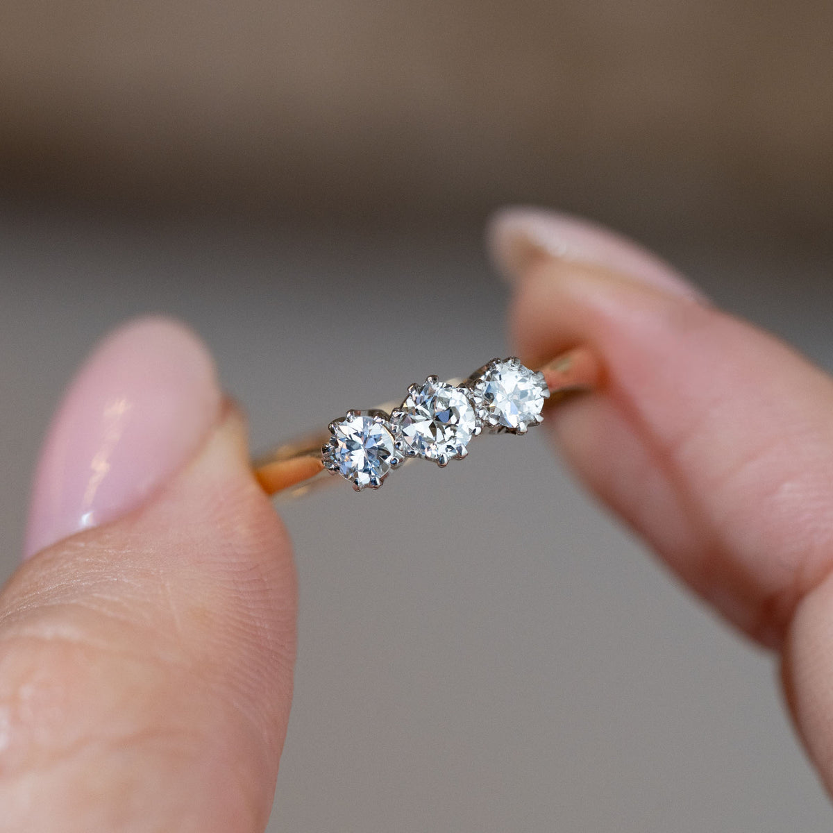 Hand-held close-up of the three sparkling old-cut diamonds, featuring a larger central stone flanked by two smaller diamonds.
