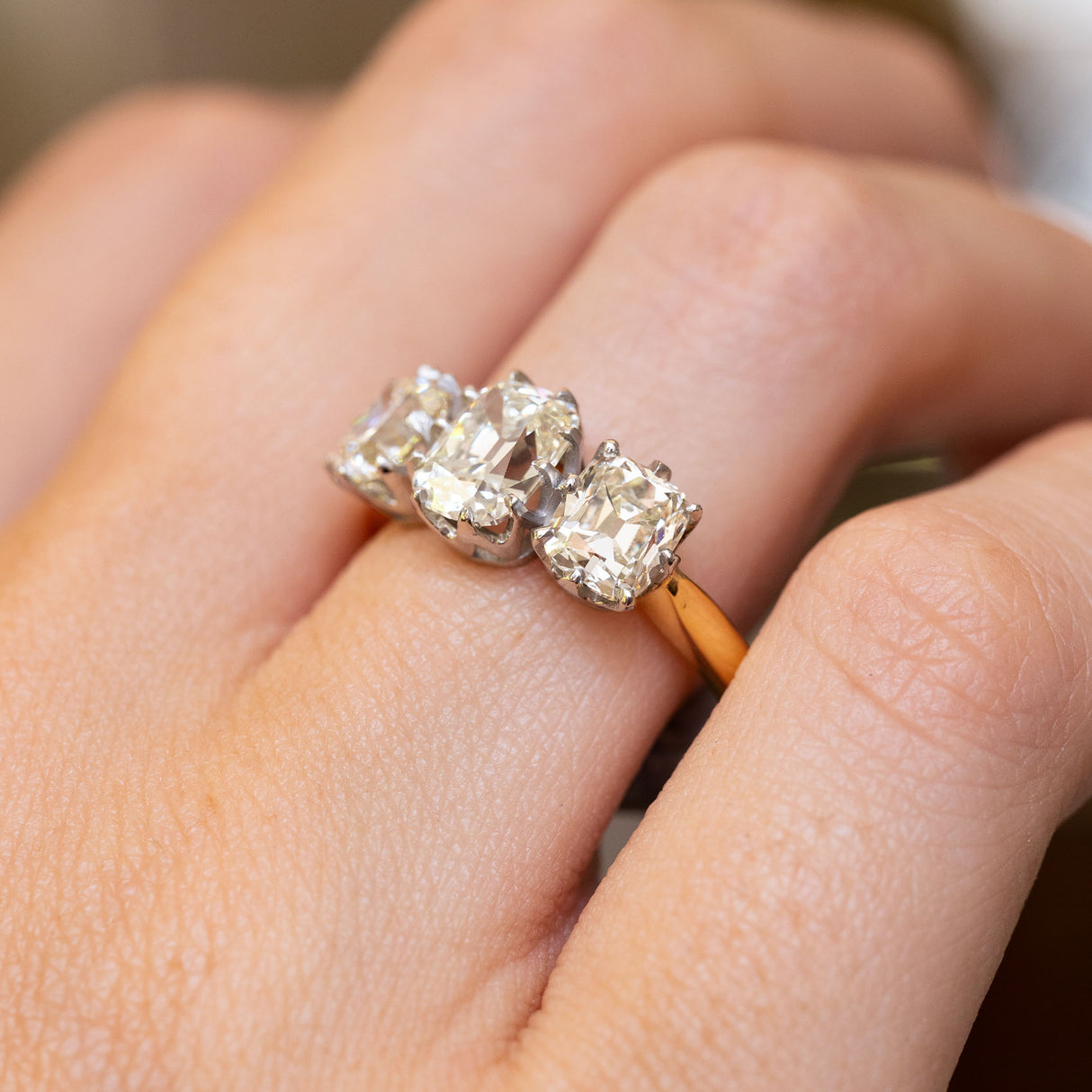 Close up of antique diamond three-stone gold engagement ring worn on the finger and pictured from an angle.