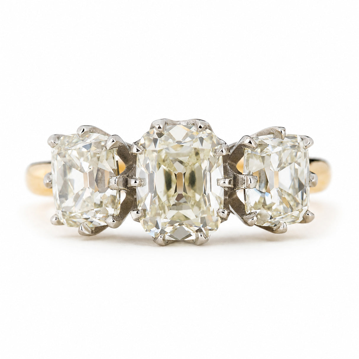 Antique old mine cut diamond trilogy ring on yellow gold band against a plain white background.