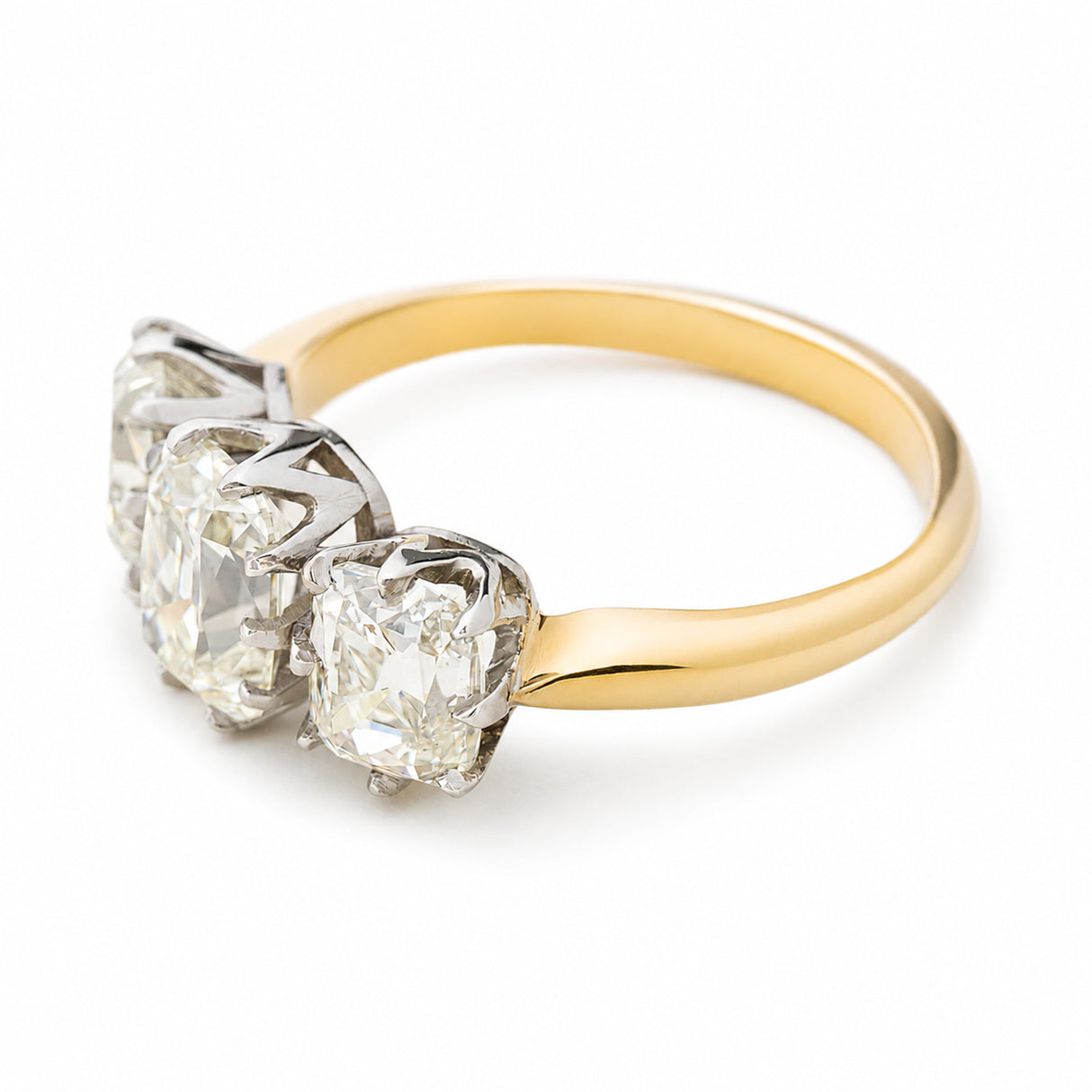 Antique old mine cut diamond three-stone engagement ring with a yellow gold band seen from above and at an angle against a plain white background.