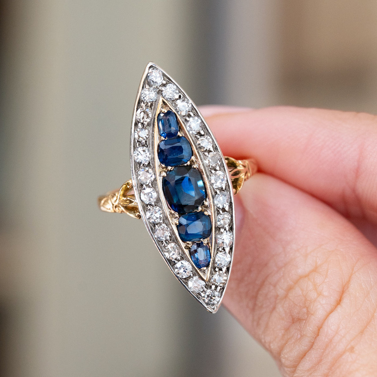 Held between the fingers, the antique navette ring showcases its silver-set diamonds, rich blue sapphires and gold accents.