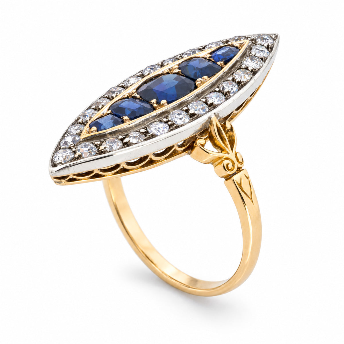 A sculptural three-quarter view reveals the elongated sapphire arrangement, diamond-set silver surround and engraved yellow gold shoulders.